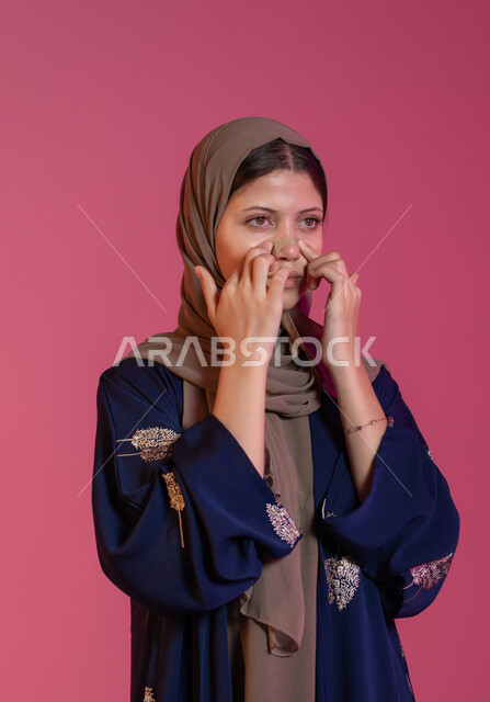 مكونات تجميلية شبابية، استخدام ماسكات تنظيف المسام, مفهوم العناية والاهتمام بنضارة وتحسين البشرة، التخلص من الرؤوس السوداء والجلد الميت، بورتريه مقرب لامرأة عربية خليجية اماراتية محجبة تقوم بوضع لصقات الأنف، خلفية وردية