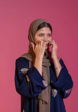 مكونات تجميلية شبابية، استخدام ماسكات تنظيف المسام, مفهوم العناية والاهتمام بنضارة وتحسين البشرة، التخلص من الرؤوس السوداء والجلد الميت، بورتريه مقرب لامرأة عربية خليجية اماراتية محجبة تقوم بوضع لصقات الأنف، خلفية وردية