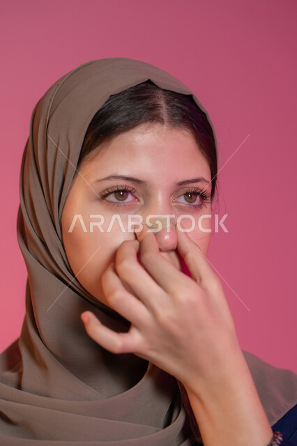 Using pore cleansing masks and feminine cosmetic ingredients, caring for and paying attention to the freshness and improvement of the skin, getting rid of blackheads and dead skin, close-up portrait of a veiled Emirati Gulf Arab woman applying nose strips, pink background
