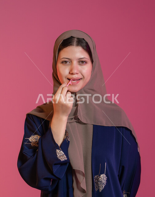 التأكد من نظافة الفم بعد تناول الطعام، الاهتمام بالأناقة والمظهر الخارجي، المحافظة على ابتسامة بيضاء، بورتريه لامرأة عربية خليجية اماراتية محجبة مبتسمة تقوم بالتنظيف باستعمال خلال أسنان بلاستيكي, خلفية وردية