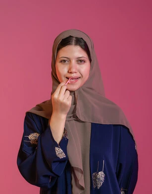 التأكد من نظافة الفم بعد تناول الطعام، الاهتمام بالأناقة والمظهر الخارجي، المحافظة على ابتسامة بيضاء، بورتريه لامرأة عربية خليجية اماراتية محجبة مبتسمة تقوم بالتنظيف باستعمال خلال أسنان بلاستيكي, خلفية وردية