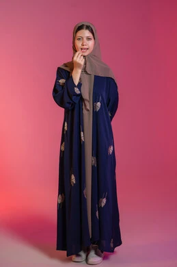 مفهوم العناية بصحة ونظافة الفم، الاهتمام بالأناقة والمظهر الخارجي، المحافظة على ابتسامة بيضاء، بورتريه لامرأة عربية خليجية اماراتية محجبة ترتدي عباءة زرقاء تقوم بتنظيف أسنانها باستعمال الخيط السني, خلفية وردية