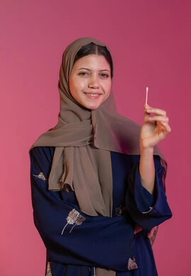 Using cotton swabs and sticks, taking care of ear health, daily ear hygiene routine, portrait of a smiling veiled Emirati Gulf Arab woman holding a cotton swab in her hand, taking care of one's appearance, pink background