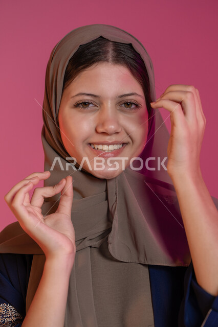 روتين نظافة الفم اليومية، تجنب التسوس وأمراض اللثة، التأكد من نظافة الأسنان بعد تناول الطعام, بورتريه لامرأة عربية خليجية اماراتية محجبة مبتسمة تقوم بالتنظيف باستعمال الخيط السني و تنظر الى الكاميرا بإيماءات السعادة والسرور, خلفية وردية