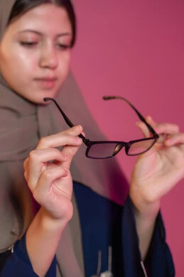 The joy of shopping and buying, correcting and improving vision, the joy of shopping in the Emirates, a blurred background of a veiled Emirati Gulf Arab woman holding medical glasses, wearing glasses for weak eyesight, taking care of one's appearance, the concept of weak eyesight
