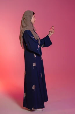 التسويق لمنتجات العطور والمستحضرات النسائية, التطيب والتعطر بالعود والزيوت العطرية, مفهوم الأناقة والاهتمام بالمظهر الخارجي, بورتريه جانبي لامرأة عربية خليجية اماراتية محجبة مبتسمة ترتدي عباءة زرقاء تقوم برش العطر، خلفية وردية