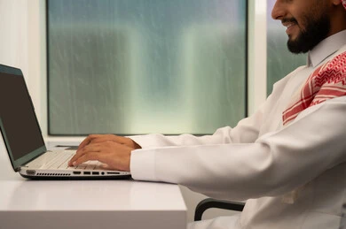 إدخال البيانات و الكتابة من خلال الكيبورد، دمج العمل مع التقنية والتكنولوجيا، مهن و وظائف مكتبية, صورة مقربة لرجل عربي خليجي سعودي يرتدي الثوب التقليدي و الشماغ و يقوم باستخدام اللابتوب