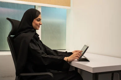 العمل على التابلت, عقد اجتماع مهني عبر الشبكة، بيئة مريحة في الشركات السعودية, مهن و وظائف مكتبية نسائية, إمرأة عربية خليجية سعودية مبتسمة ترتدي عباءة سوداء و تمسك جهاز لوحي