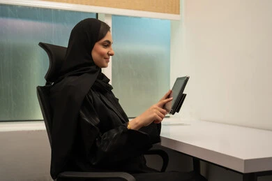 Organizing an electronic meeting, a comfortable work environment in Saudi companies, professions and office jobs for women, a smiling Arab Gulf Saudi woman wearing a black abaya with a tablet in front of her, the concept of accomplishing tasks.