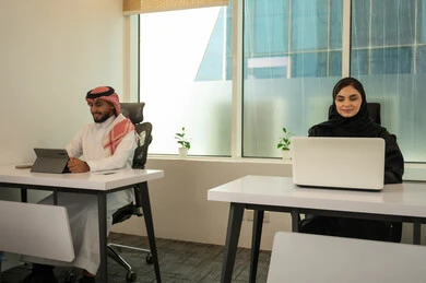 العمل في بيئة مكتبية حديثة، ايماءات السعادة والاندماج، الروح التشاركية و المحادثات العامة، الخطط الاستراتيجية لتحقيق الأهداف، نمط الحياة في الشركات السعودية، فريق عربي خليجي سعودي مكون من رجل يرتدي الثوب التقليدي و الشماغ و سيدة محجبة ترتدي العباءة السوداء, انجاز المهام من خلال اللابتوب و التابلت