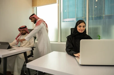 الاشارة الى الجهاز اللوحي, الإشراف على المشاريع في مقر العمل، تعزيز الروح التشاركية، توزيع المهام المطلوبة لتطوير أهداف الشركة, نمط الحياة في الشركات السعودية، فريق عربي خليجي سعودي مكون من رجلين يرتديان الثوب التقليدي و الشماغ و سيدة محجبة ترتدي العباءة السوداء, انجاز المهام من خلال اللابتوب و التابلت