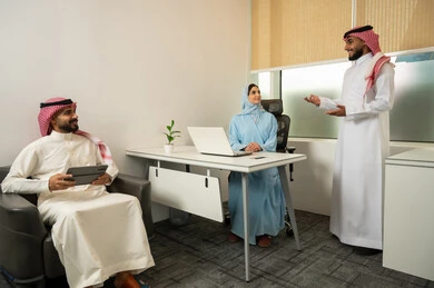 توضيح بنود الصفقات الجديدة، بيئة عمل السعودية, فريق عربي خليجي سعودي مكون من رجلين يرتديان الثوب التقليدي و الشماغ و سيدة محجبة ترتدي العباءة الزرقاء تستخدم اللابتوب,  دمج الأعمال مع التقنية و التكنولوجيا, نقاشات و محادثات عامة