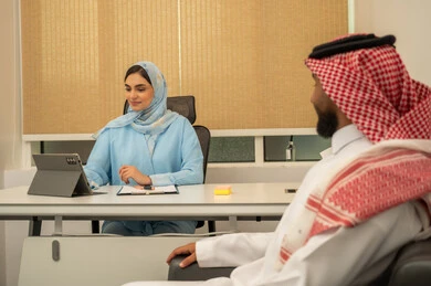 دراسة جدوى الأعمال، مراجعة نتائج الاجتماع، مهن ووظائف ادارية, العمل الجماعي و التعاون، فريق عربي خليجي سعودي مكون من رجل يرتدي الثوب التقليدي و الشماغ و سيدة محجبة ترتدي العباءة الزرقاء و أمامها جهاز التابلت, تنظيم و إعداد التقارير اليومية