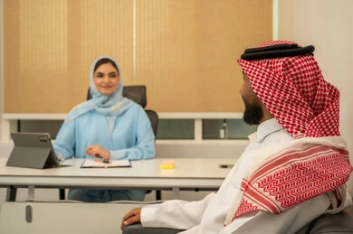 تنظيم و إعداد التقارير اليومية، دراسة جدوى الأعمال، مراجعة نتائج الاجتماع، مهن ووظائف ادارية, العمل الجماعي و التعاون، فريق عربي خليجي سعودي مكون من رجل يرتدي الثوب التقليدي و الشماغ و سيدة محجبة ترتدي العباءة الزرقاء و أمامها جهاز التابلت