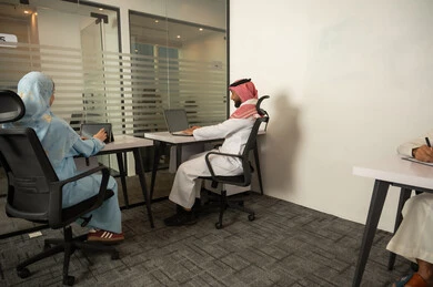 تحسين جودة العمل و خطط التطوير, نمط الحياة في الشركات السعودية، فريق عربي خليجي سعودي مكون من رجل يرتدي الثوب التقليدي و الشماغ و سيدة محجبة ترتدي العباءة الزرقاء, انجاز المهام من خلال اللابتوب و التابلت