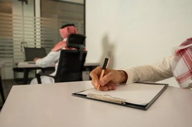 دراسة و تتبع المشاريع، ملفات و وثائق خاصة بالعمل، الاحترافية والتفاني في الإنجاز، تسجيل الملاحظات و النتائج, صورة مقربة ليد رجل عربي خليجي سعودي يرتدي الثوب التقليدي و يقوم بالكتابة على ورق أبيض, مهن و وظائف مكتبية, الحياة المهنية السعودية