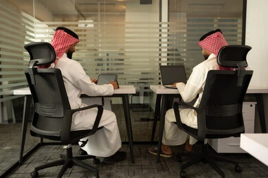 الاستعانة بالأجهزة التقنية الحديثة، إتمام المهام في المكتب، تطور الشركات السعودية, العمل الجماعي و التعاون، رجلان عربيان خليجيان سعوديان يرتديان  الثوب التقليدي و الشماغ و يقومون باستخدام اللابتوب و التابلت, الجلوس على كرسي مريح
