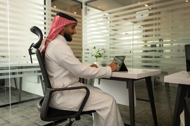 مهنة و وظيفة سعودية مكتبية, إتمام مهام العمل في المكتب،  موظف عربي خليجي سعودي يرتدي الثوب التقليدي و الشماغ و يقوم باستخدام التابلت, دمج التقنية و الأجهزة الحديثة مع الحياة العملية, ايماءات الاندماج و التركيز