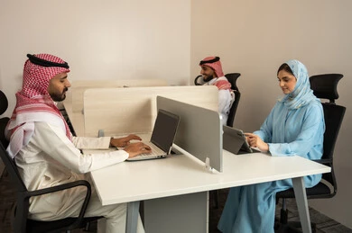 الشركات و المكاتب في المملكة العربية السعودية، إدارة شؤون الأعمال و تنظيمها،  العمل الجماعي و التعاون، فريق عربي خليجي سعودي مكون من رجلين يرتديان الثوب التقليدي و الشماغ و سيدة محجبة ترتدي العباءة الزرقاء و يقومون باستخدام اللابتوب و التابلت, ايماءات الاندماج و التركيز