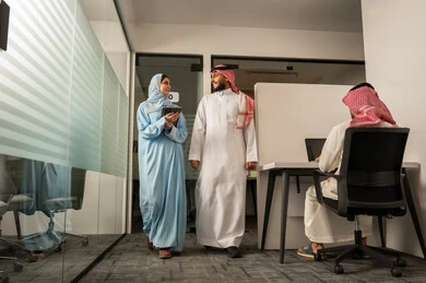 شرح واضح للأعمال, نقاش و حوار في بيئة مكتبية, استخدام الجهاز اللوحي لتوضيح العمليات المتبعة، التفاهم والتعاون بين الزملاء لتحقيق أهداف الشركة، مهن ووظائف إدارية، فريق عربي خليجي سعودي مكون من رجل يرتدي الثوب التقليدي و الشماغ و سيدة محجبة ترتدي العباءة الزرقاء و تتحدث مع زميلها