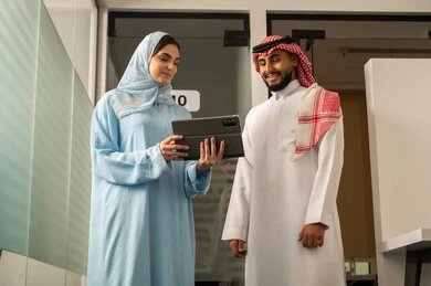 توضيح اهداف وسياسة الشركة، الحوار و التفاهم بين الموظفين, مهن ووظائف مكتبية، فريق عربي خليجي سعودي مكون من رجل يرتدي الثوب التقليدي و الشماغ و سيدة محجبة ترتدي العباءة الزرقاء و تشرح استيراتيجية العمل لزميلها باستخدام التابلت,  ضمان فهم واضح و شامل للاعمال