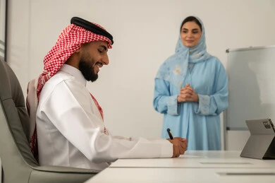 كتابة و تدوين شيء ما, مناقشة عمل بين الزملاء, مهن ووظائف ادارية,  العمل الجماعي و التعاون، فريق عربي خليجي سعودي مكون من رجل يرتدي الثوب التقليدي و الشماغ و سيدة محجبة ترتدي العباءة الزرقاء و تشرح الاستيراتيجية لزميلها, دراسة المشاريع الجديدة في شركات المملكة العربية السعودية