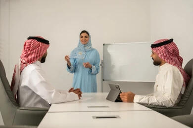 جمع البيانات و حل المشكلات، تطوير و دراسة المشاريع الجديدة, توضيح العمليات و الاجراءات المتبعة في الشركة، العمل الجماعي و التعاون، فريق عربي خليجي سعودي مكون من رجلين يرتديان الثوب التقليدي و الشماغ و سيدة محجبة ترتدي العباءة الزرقاء و تشرح لزملائها باستعمال السبورة, استخدام التابلت في تدوين الملاحظات