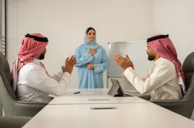 Meeting and discussion at the company headquarters, data collection and problem-solving, teamwork and collaboration, a Gulf Arab Saudi team consisting of two men wearing traditional thob and ghutrah and a veiled woman wearing a blue abaya explaining to her colleagues using a whiteboard, using a tablet to take notes.