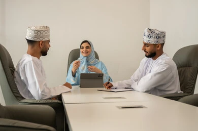 تنظيم وادارة جدول مفهوم العمل, بيئة العمل المريحة في الشركة عمانية, شرح المهام المطلوبة بسعادة وحب, التعاون والتفاهم بين الفريق, تبادل الخبرات والاتفاقيات الناجحة, فريق عمل عربي خليجي عماني مكون من رجلين يرتديان الدشداشة و الكمة و سيدة محجبة ترتدي عباءة زرقاء و تستخدم التابلت