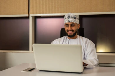 الضغط على مفاتيح الكيبورد، دمج العمل مع التقنية والتكنولوجيا، إدارة شؤون الأعمال وتنظيمها عبر الأجهزة الحديثة، رجل عربي خليجي عماني يرتدي الدشداشة و الكمة يقوم باستخدام اللابتوب, مفهوم إنجاز المهام عن بعد, بيئة العمل المكتبي المريح