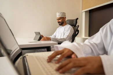 Having the skill of fast typing on the keyboard, a close-up image of the hands of an Arab Gulf Omani man wearing a dishdasha using a laptop, the concept of remote work, data entry through the keyboard, integrating work with technology and tech.