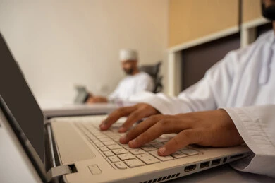 إدخال البيانات من خلال لوحة المفاتيح، دمج العمل مع التقنية والتكنولوجيا، امتلاك مهارة الكتابة السريعة على الكيبورد، صورة مقربة لأيدي رجل عربي خليجي عماني يرتدي الدشداشة يقوم باستخدام اللابتوب, مفهوم العمل عن بعد