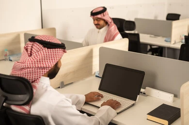 Arab Saudi Gulf colleagues are using laptops, designated spaces for each employee in the company, focus and meticulous work, dialogues and discussions within the team, business and company development, work meetings and project completion, discussing plans and explaining work tasks.