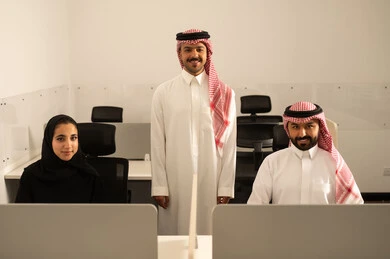 Explanation and sharing of experiences among colleagues, focus and meticulous work, dialogues and discussions within the team, business and company development, work meetings and project completion, discussing plans and explaining work tasks, Arab Saudi Gulf colleagues wearing traditional attire and the ghutrah exchanging conversation.