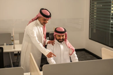 Work meeting and project completion, explaining and sharing experiences among colleagues, focus and meticulous work, dialogues and discussions within the team, business and company development, discussing plans and explaining work tasks, Arab Saudi Gulf colleagues wearing traditional attire and shemagh exchanging conversation.