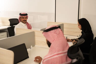 Discussion of plans and explanation of work tasks, designated places for each employee in the company, focus and meticulous work, dialogues and discussions within the team, business and company development, work meetings and project completion, Arab Saudi Gulf colleagues using laptops.
