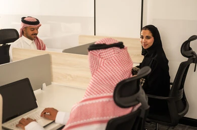 Focus and meticulous work, designated spaces for each employee in the company, dialogues and discussions within the team, business and company development, work meetings and project completion, discussing plans and explaining work tasks, Arab Saudi Gulf colleagues using laptops.