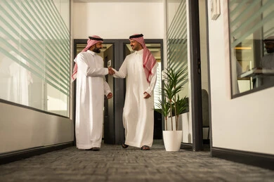 Two Saudi Arabian Gulf Arab employees stand with gestures of happiness, the concept of dialogue and exchanging opinions in business achievement plans, administrative office professions and jobs, discussing project plans, explaining work tasks, dialogues and discussions within the team, business and company development.