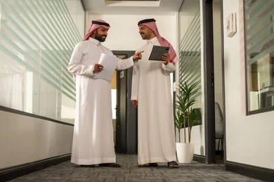 Business and company development, using tablets and laptops to accomplish tasks, focus and meticulous work, dialogues and discussions within the team, Arab Gulf Saudi employees sitting in the office, discussing project plans, explaining business tasks.