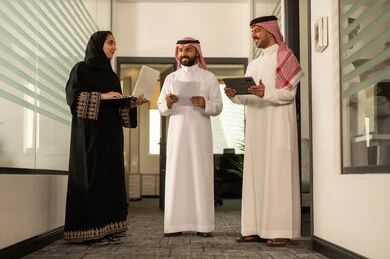 Using a tablet and a laptop to accomplish tasks, focus and meticulous work, dialogues and discussions within the team, business and company development, Arab Gulf Saudi employees sitting in the office, discussing project plans, explaining business tasks.