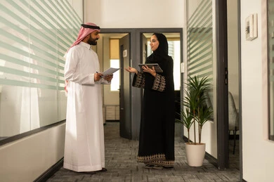 Using a tablet to accomplish tasks, focus and meticulous work, dialogues and discussions within the team, business and company development, Arab Gulf Saudi employees sitting inside the office, discussing project plans, explaining business tasks.