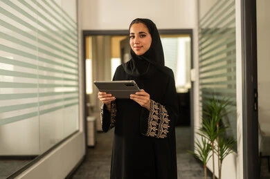 The concept of business management and achieving company goals, professions and office jobs, an Arab Gulf Saudi employee wearing an abaya and hijab working on a tablet, completing work tasks remotely.