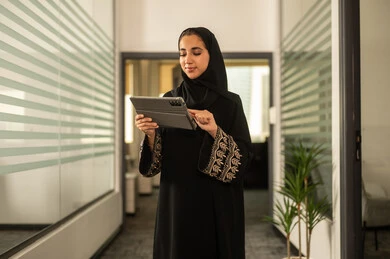Office professions and jobs, the concept of business management and achieving company goals, a Gulf Arab Saudi female employee wearing an abaya and hijab working on a tablet, completing work tasks remotely.