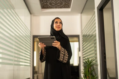 موظفه عربيه خليجيه سعوديه ترتدى العباءه والحجاب تعمل على الجهاز اللوحى، انجاز مهام العمل عن بعد، مهن ووظائف مكتبية ، مفهوم ادارة الاعمال وتحقيق اهداف الشركة