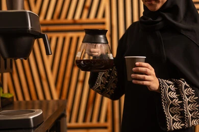 غرفة استراحة العمل ، مهن ووظائف نسائية ، العمل في القطاع الإداري والمكتبي، امراه عربيه خليجيه سعوديه ترتدي العباءه والحجاب تستخدم اله تحضير القهوة السريعة، منتج وطني محلي سعودي، الاستمتاع باعداد المشروبات الساخنة الطازجة