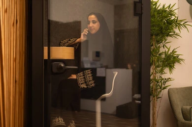 Integrating advanced technologies in the workplace, checking on family and friends, an Arab Gulf Saudi woman wearing an abaya and hijab sitting in the work break room using a mobile phone, professions and jobs for women, working in the administrative and office sector.