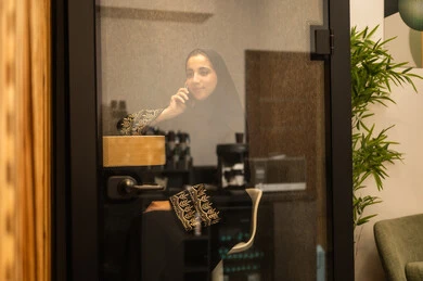 Integrating advanced technologies in the workplace, checking on family and friends, an Arab Gulf Saudi woman wearing an abaya and hijab sitting in the work break room using a mobile phone, professions and jobs for women, working in the administrative and office sector.