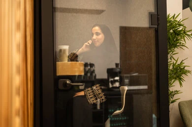 Integrating advanced technologies in the workplace, checking on family and friends, an Arab Gulf Saudi woman wearing an abaya and hijab sitting in the work break room using a mobile phone, professions and jobs for women, working in the administrative and office sector.