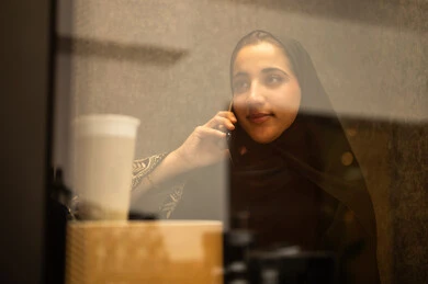 دمج التقنيات المتطورة فى العمل ، الاطمئنان على الاهل والاصدقاء ، امراه عربيه خليجيه سعوديه ترتدي العباءه والحجاب تجلس فى غرفة استراحة العمل تستخدم الهاتف المحمول ، مهن ووظائف نسائية ، العمل في القطاع الإداري والمكتبي