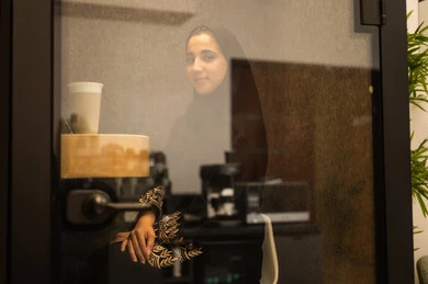 Women's professions and jobs, working in the administrative and office sector, break room, an Arab Gulf Saudi woman wearing an abaya and hijab using a quick coffee maker, a local Saudi national product, enjoying preparing fresh hot beverages.